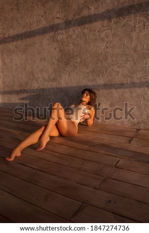 young girl with long legs in beige body lies fashion and elegant on the floor in sun lights near gray wall background, lifestyle concept, free space