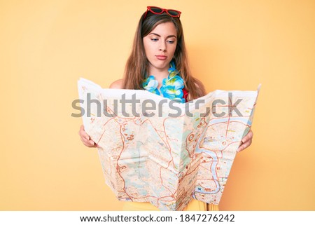 Beautiful young caucasian woman wearing bikini and holding city map thinking attitude and sober expression looking self confident 