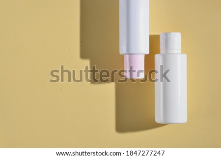 Cream tube on bright sunny yellow background with pink peony flower. Cosmetic skincare product blank plastic package. White unbranded lotion, balsam, hand creme, toothpaste mockup. Selected focus

