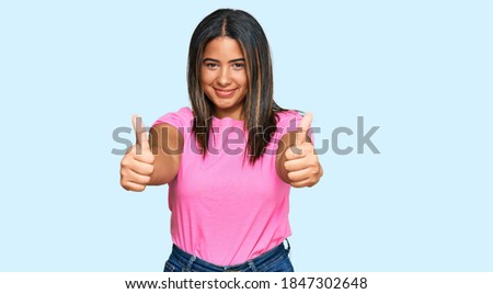 Young latin girl wearing casual clothes approving doing positive gesture with hand, thumbs up smiling and happy for success. winner gesture. 
