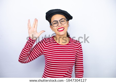 Young beautiful brunette woman wearing french beret and glasses over white background doing hand symbol