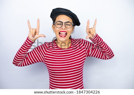 Young beautiful brunette woman wearing french beret and glasses over white background shouting with crazy expression doing rock symbol with hands up