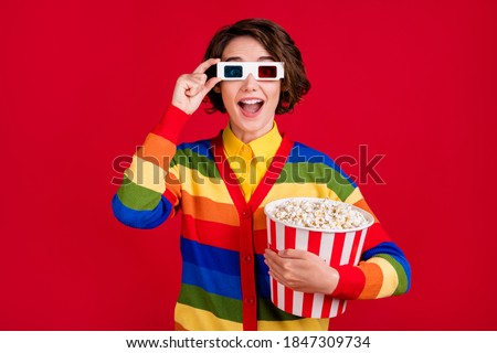 Photo of pretty funny lady hold big popcorn bucket watch movie cinema premiere nice picture quality wear 3d spectacles striped cardigan jumper isolated bright red color background
