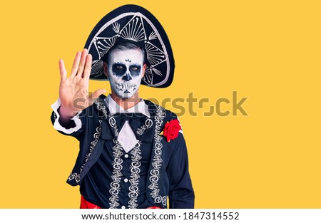 Young man wearing day of the dead costume over background doing stop sing with palm of the hand. warning expression with negative and serious gesture on the face. 