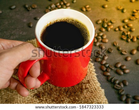 The picture of red cup of warm hot black coffee with froths on coffee and and coffee beans,powder on a sack of hemp.