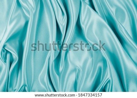 Photography of beautiful wavy turquoise silk satin luxury cloth fabric, abstract background design.