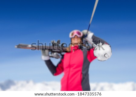 A medium shot of a young woman holding skis with selective focus on a ski pole.