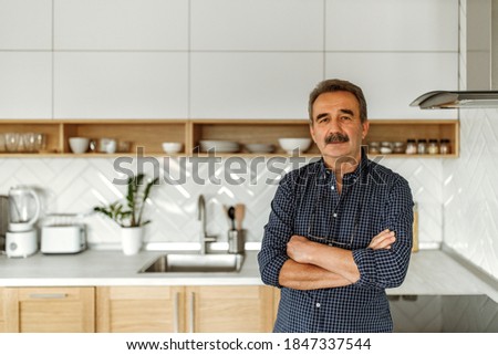 Adult man with crossed hands standing in front of his kitchen.
