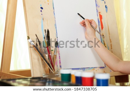artist's hand holds paint brush on the background of the easel