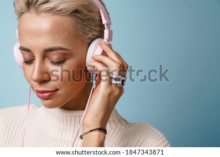 Relaxed beautiful girl listening music with headphones isolated over blue background