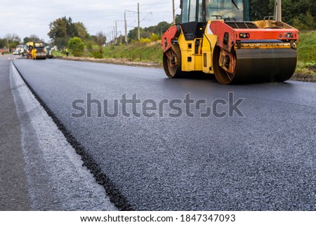 Asphalt road roller with heavy vibration roller compactor press new hot asphalt on the roadway on a road construction site. Heavy Vibration roller at asphalt pavement working. Repairing. Royalty-Free Stock Photo #1847347093