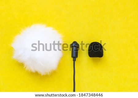 Lavalier small microphone and wind protection on yellow background.