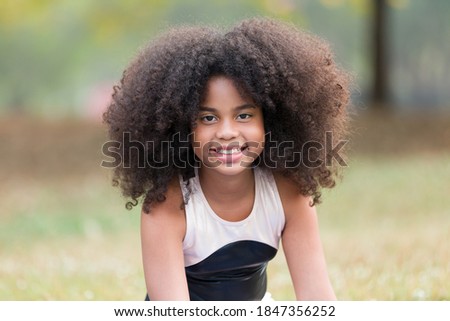 Portrait of happy smiling African American little girl doing yoga outdoor. Little afro girl with curly hairstyle practicing yoga in the park