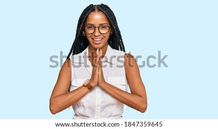 Beautiful hispanic woman wearing casual clothes and glasses praying with hands together asking for forgiveness smiling confident. 