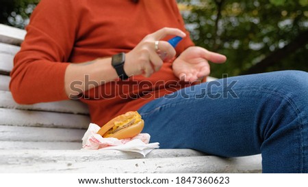 A young guy disinfects his hands from germs with a spray before eating food. Protection, personal hygiene. Hamburger snack on the street. Royalty-Free Stock Photo #1847360623