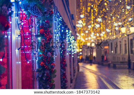 Windows of the house are decorated with balls and garlands during the celebration of the new year. City street with night lantern lights