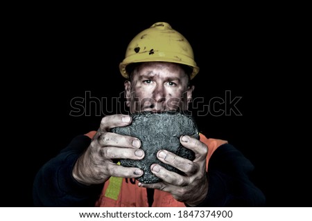A coalminer holds out a large chunk of energy rich coal in a dark coalmine. Royalty-Free Stock Photo #1847374900