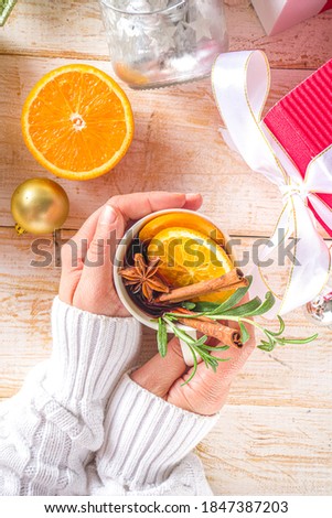 Traditional Winter Hot Alcohol Drink. Mulled Wine in a white Cup on the background of the kitchen table with Christmas decorations. Girl Hands in pic Holds Mulled Wine Mug