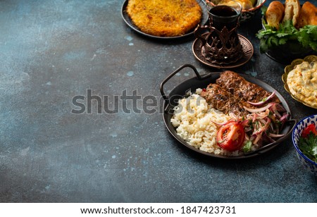 Traditional Turkish dish meat kebab with rice, vegetables with appetizers and Turkish tea in glass. Kebab, eggplant sauce, pita bread, dessert Künefe and baklava. Middle Eastern meal, copy space