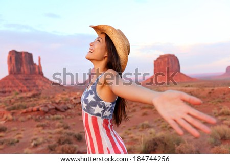 Cowgirl - woman happy and free in Monument Valley wearing cowboy hat with arms outstretched in freedom concept. Beautiful smiling multiracial young woman outdoors, Arizona Utah, USA.