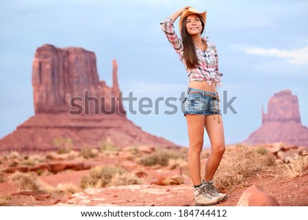 Cowgirl woman tourist travel in Monument Valley wearing cowboy hat and hiking shoes. Beautiful smiling multiracial young woman outdoors, Arizona Utah, USA.
