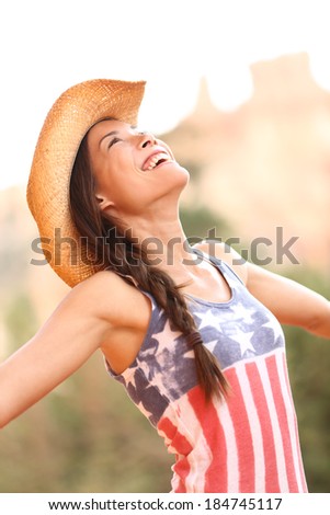 American cowgirl woman free and happy wearing cowboy hat outdoors in countryside. Cheerful elated joyful woman smiling enjoying freedom. Beautiful mixed race Asian Caucasian female model.