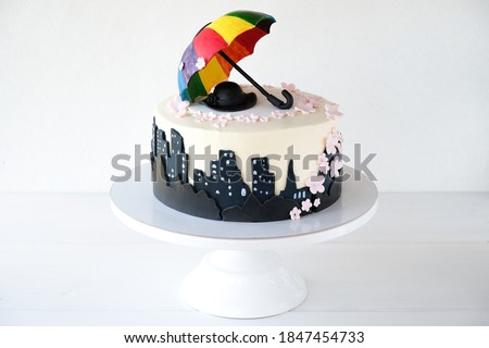
Birthday cake decorated with city silhouette, colorful umbrella, hat and flowers Royalty-Free Stock Photo #1847454733