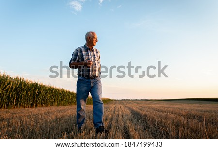 Portrait of senior farmer walking in field at sunset.