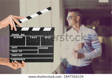 Hands holding film clapper board with an actor on background