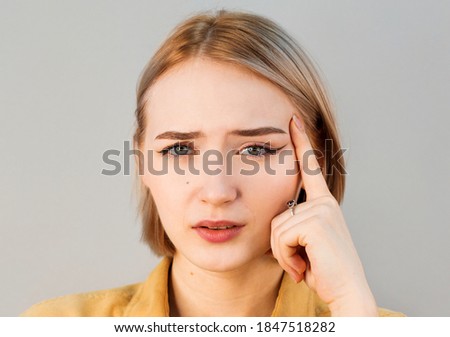 Horizontal portrait of displeased woman with blonde hair has indignant expression of face, frowns eyebrows, cant understand something. Attractive puzzled dissatisfied female keeps hand on chin