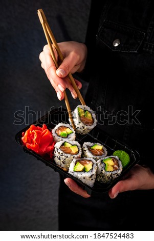 Woman eating delivered at home sushi from a container with japanese sticks