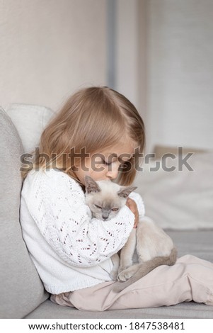 Little girl hugging a kitten on sofa.