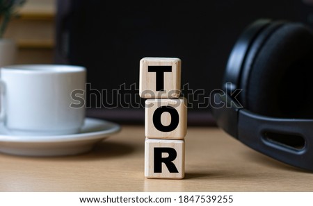 TOR (The Onion Router) -word on cubes on the background of the tablet, headphones and a white cup. Technology and computers concept.
