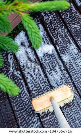Brush and canister of detergent on a wooden deck. Technologies and tools for cleaning surfaces and a spruce twig Royalty-Free Stock Photo #1847556916