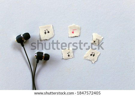 Earphones with musical notes drawed on small pieces of paper, representing music being played.