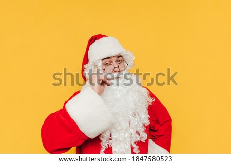 A smart Santa Claus looks at the camera and shows a "think about it" gesture touching his finger to his temple, isolated on a yellow background.
