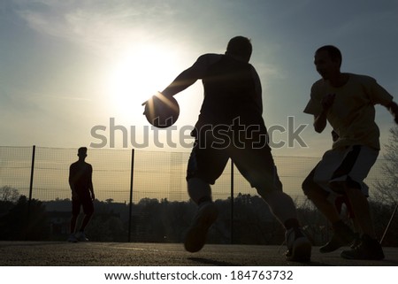 Basketball player silhouettes playing on an outdoor court as the sun creates a flare by the ball