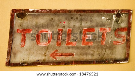 old rustic sign showing way to toilets on yellow wall with red lettering