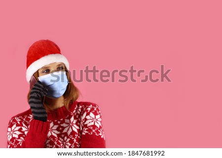 A young girl in santa claus hat and medical protective mask speaks on the phone