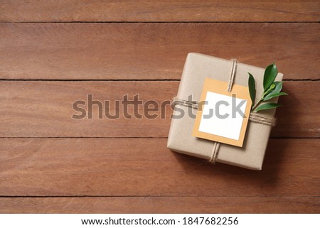 empty card on gift box wrapped in recycled paper with rope and leaf on wood background with copy space for text or image / green concept
