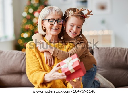 Happy family on Christmas morning. Affectionate grandmother and cheerful granddaughter open a holiday gift together at home
