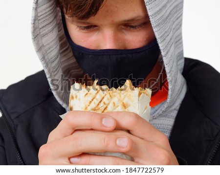 portrait of a teenager in a mask eating fast food