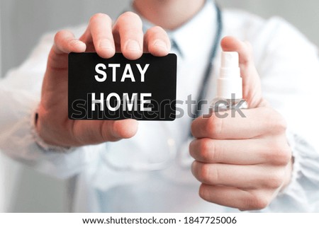 Doctor holding a paper black card with text STAY HOME and the medicine bottle, medical concept. The label is made in white text