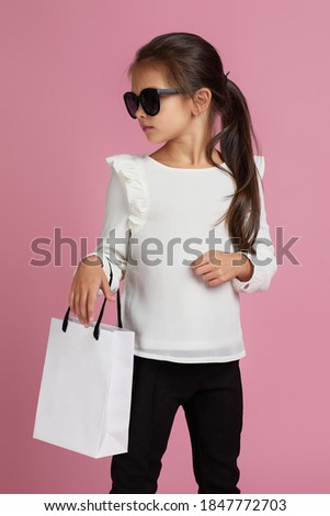Sale. cute fashionable elegant little child girl in sunglasses is holding shopping bag on pink background.