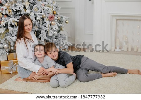 portrait of a beautiful young woman and two boys against the background of a New Year tree. Mom and sons. Christmas and New Year concept.