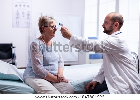 Measuring old senior woman temperature during consultation in clinic examination room. Medical consultation for infections and disease during global pandemic,flu, tool, sickness.