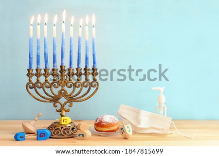 Image of jewish holiday Hanukkah with menorah (traditional Candelabra), donut, wooden dreidel (spinning top). Coronavirus prevention concept, medical mask and and sanitizer gel