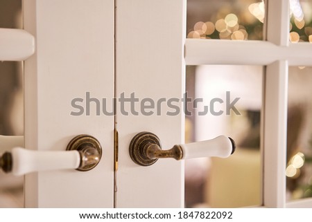 Beautiful modern door knob. Christmas lights on the background. Open, wooden front door from the interior of an upscale home with windows.