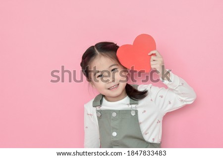 little girl holding red heart on pink background