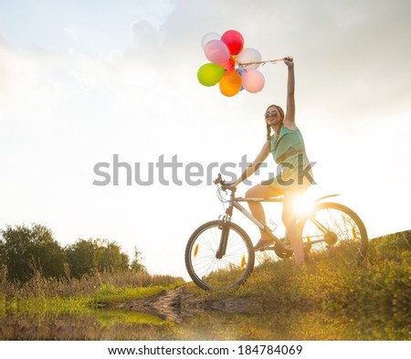 Girl with sunglasses riding bicycle, flying balloons on leash.